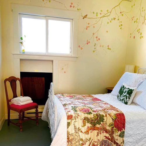 Cozy bedroom with a floral quilt, a chair, and a window adorned with nature-themed wall art.