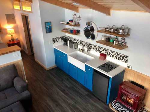 A modern kitchen with blue cabinets, a farmhouse sink, and a red stove, featuring open shelves and stylish decor.