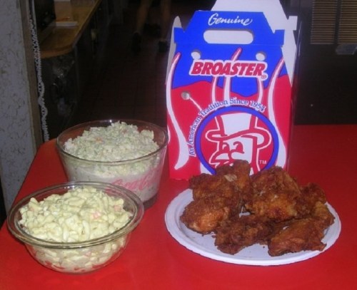 A plate of fried chicken with two bowls of coleslaw and macaroni salad, next to a branded takeout box.