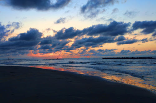 A serene beach at sunset, with colorful clouds reflecting on the water and gentle waves lapping at the shore.