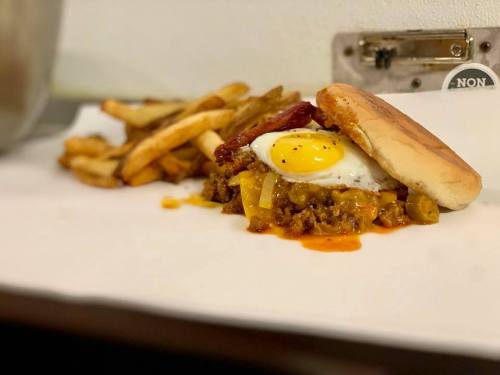 A burger with a fried egg and savory toppings, served with a side of crispy French fries on a white surface.