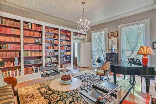 Cozy room with a grand piano, bookshelves filled with books, elegant chandelier, and stylish furniture.