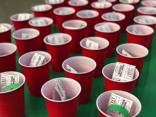 A table filled with red plastic cups, each containing a ticket and a green wristband.