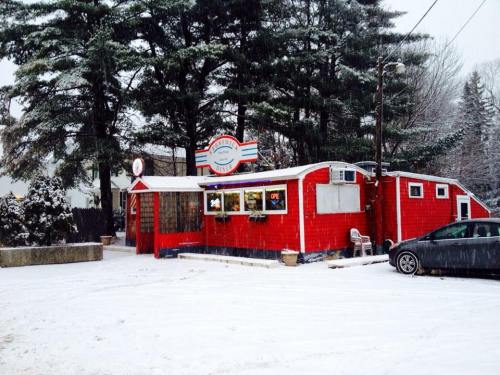 A red diner in a snowy landscape, featuring a sign and large windows, with a car parked nearby.