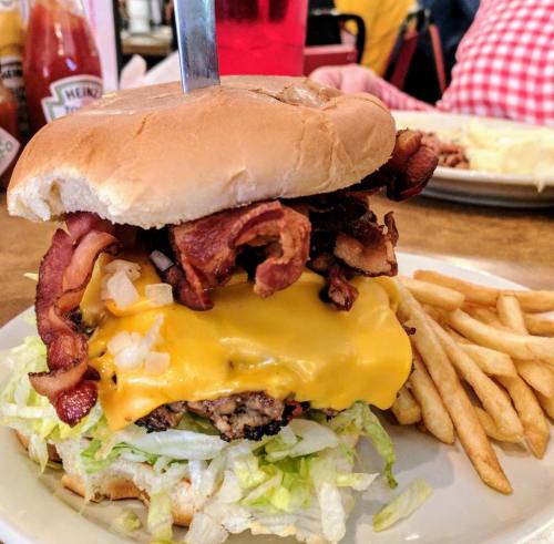 A towering cheeseburger with bacon, lettuce, and onion, served with fries on a plate.