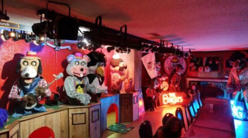 A colorful restaurant stage featuring animatronic characters performing, with neon signs and a lively atmosphere.