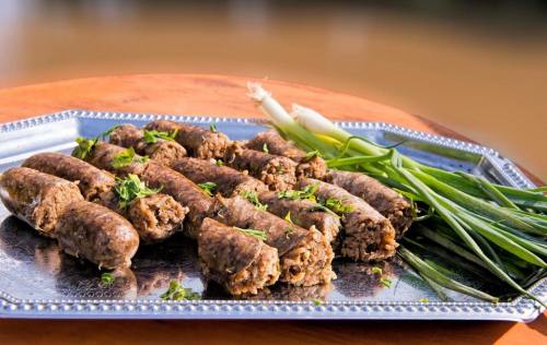 A silver platter with rolled meat sausages garnished with green onions and herbs.
