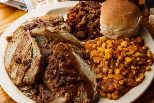 A plate of sliced roast beef with gravy, corn, pecan pie, and a dinner roll.