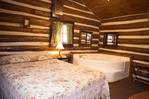 Cozy log cabin interior featuring a floral bedspread, a jacuzzi tub, and rustic wooden walls.