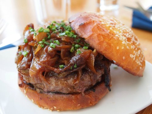 A juicy burger topped with caramelized onions and chopped chives, served on a sesame seed bun.