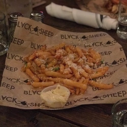 A plate of fries topped with cheese and herbs, served with a side of dipping sauce, on branded paper.
