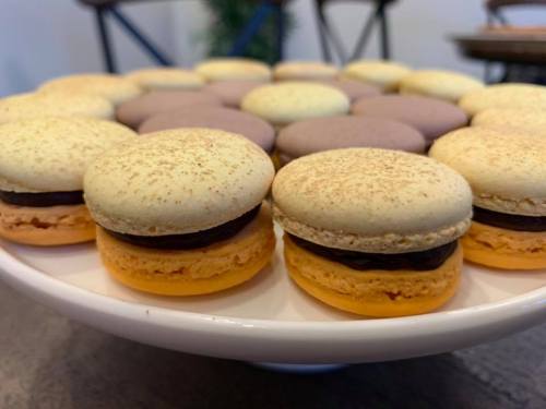 A plate of colorful macarons in various flavors, featuring yellow, purple, and beige shells with chocolate filling.