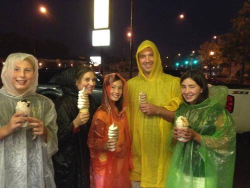 A group of five people in colorful ponchos holding ice cream cones on a rainy night.