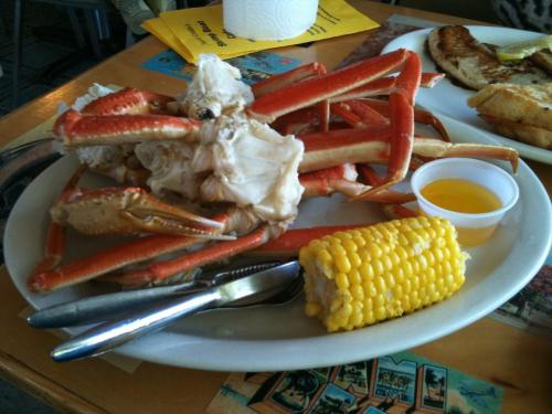 A plate with a large crab, a side of corn on the cob, and a small cup of melted butter.