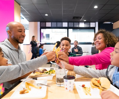 A family enjoys a meal together, sharing fries and smiling in a vibrant restaurant setting.