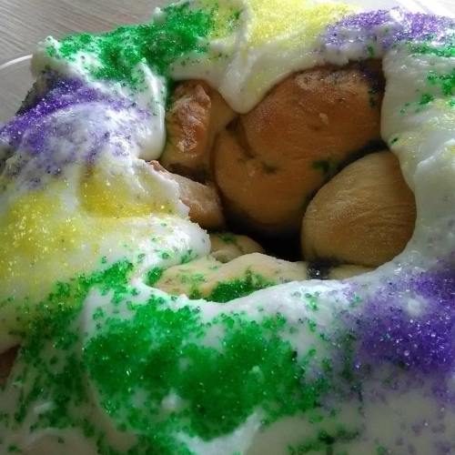 A colorful king cake topped with purple, green, and yellow sugar, featuring a creamy icing.