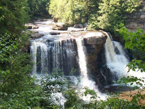 A scenic waterfall cascading over rocky cliffs, surrounded by lush green trees and a tranquil river below.