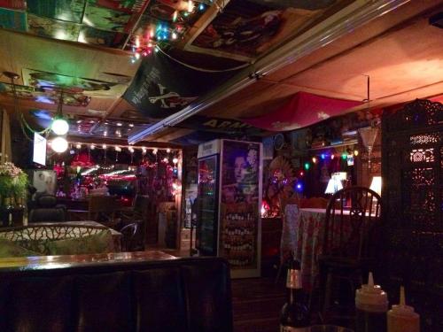 Cozy, dimly lit restaurant with colorful lights, flags, and vintage decor, featuring tables and a fridge in the background.