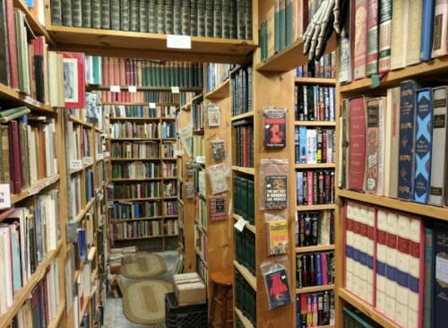 A narrow aisle lined with bookshelves filled with various books in a cozy, cluttered bookstore.