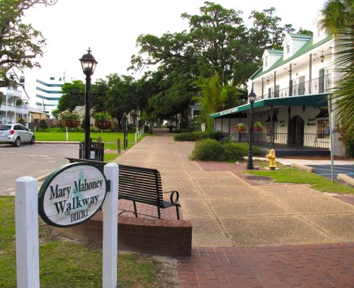 A scenic walkway named Mary Mahoney, featuring benches, greenery, and nearby buildings in a peaceful setting.