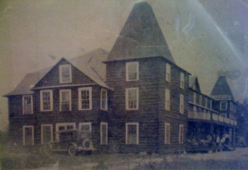 Historic wooden building with a steep roof, featuring multiple windows and a vintage car parked in front.