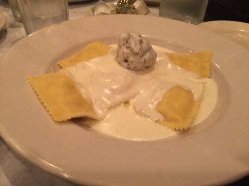 Plate of ravioli topped with creamy sauce and a dollop of ricotta, served in a restaurant setting.