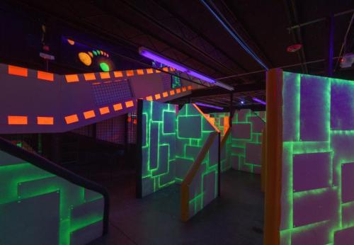 A vibrant indoor space with glowing neon walls and colorful lighting, featuring ramps and barriers for an engaging activity.