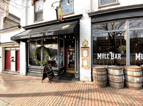 Exterior of a restaurant named "Twisted Comfort Food" with a festive wreath and a nearby bar called "Mule Bar."