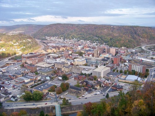 Aerial view of a city surrounded by hills, featuring buildings, roads, and a mix of urban and natural landscapes.