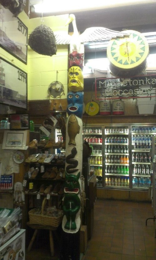 A colorful totem pole with various painted faces and animals, surrounded by souvenirs and a display of beverages.