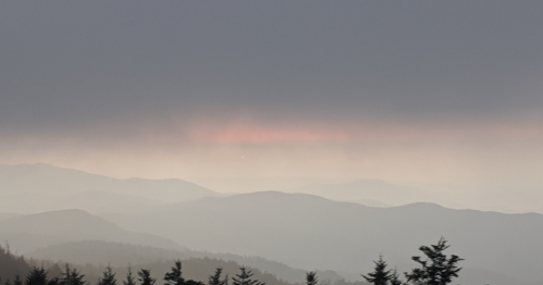 A hazy mountain landscape at dusk, with soft pink hues in the sky and silhouettes of distant peaks.