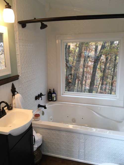 A cozy bathroom featuring a bathtub, sink, and a large window with a view of trees outside.
