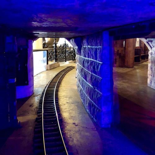 A curved train track runs through a dimly lit space with blue lighting and stone walls.