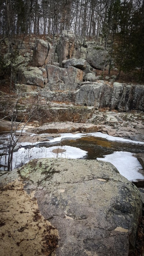 Rocky landscape with a frozen stream and sparse trees in a winter setting.