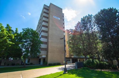 A tall brick building surrounded by trees and greenery under a clear blue sky.