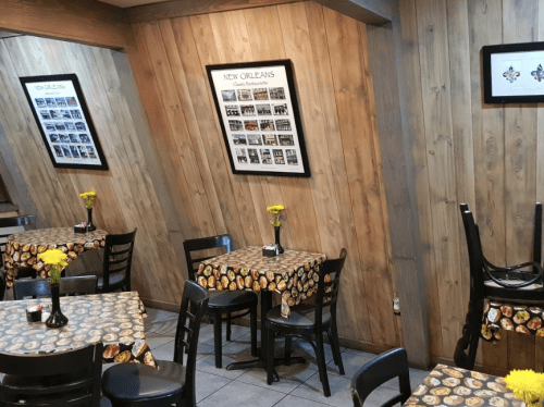 Cozy restaurant interior with wooden walls, tables covered in patterned cloth, and yellow flowers in vases.