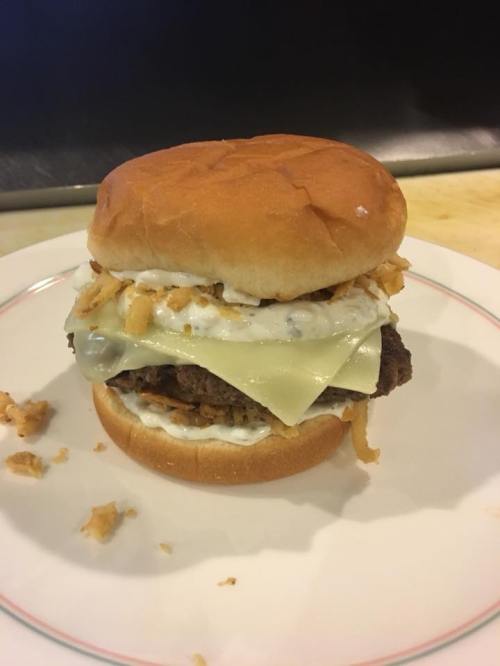 A burger with a beef patty, melted cheese, crispy onions, and creamy sauce, served on a toasted bun.