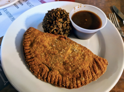 A plate with a golden-brown empanada, a scoop of rice, and a small cup of sauce.