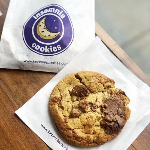 A chocolate chip cookie on a branded paper wrapper from Insomnia Cookies, resting on a wooden surface.