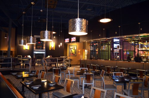 Modern restaurant interior with dark walls, stylish lighting, and empty tables arranged for dining.