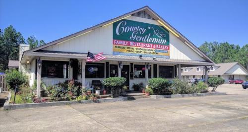 Exterior of Country Gentleman Family Restaurant & Bakery, featuring a sign and American flag, surrounded by greenery.