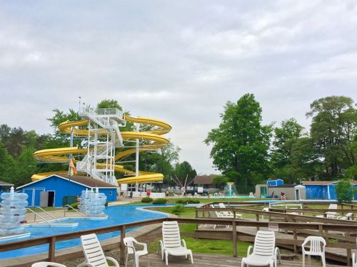 A water park scene featuring a yellow waterslide, a pool, and lounge chairs under a cloudy sky.