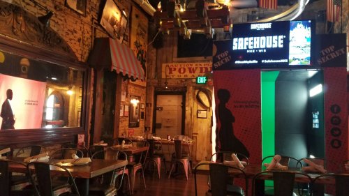 Interior of a themed restaurant with eclectic decor, featuring tables, a large screen, and a secretive entrance.