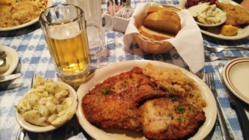 A plate of fried chicken with sauerkraut, macaroni salad, and a glass of beer, set on a checkered tablecloth.