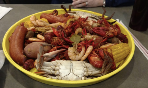 A vibrant seafood platter featuring shrimp, crab, crawfish, sausage, corn, and potatoes on a yellow tray.