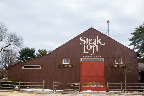 A rustic wooden barn with "Steak Loft Restaurant" sign, featuring doors labeled "Luncheon" and "Dinner."