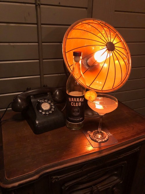 A vintage scene featuring a cocktail, a bottle of Havana Club rum, an old telephone, and a glowing lamp.