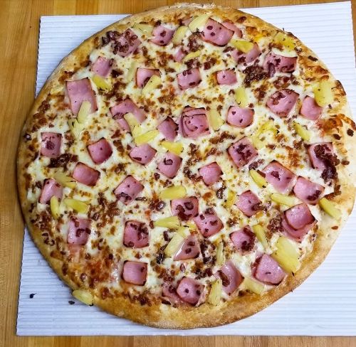 A round pizza topped with cheese, ham, and pineapple chunks on a white surface.
