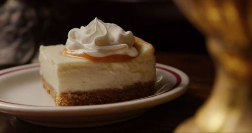 A slice of cheesecake topped with whipped cream and a drizzle of caramel, served on a small plate.