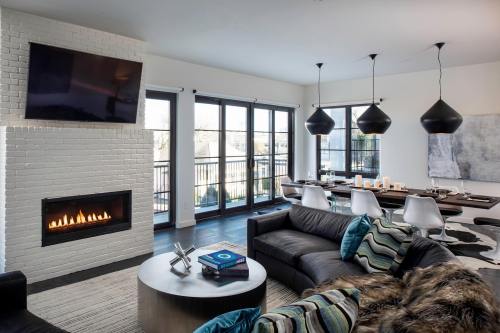 Modern living room with a fireplace, large windows, and stylish furniture, featuring a dining area and contemporary decor.